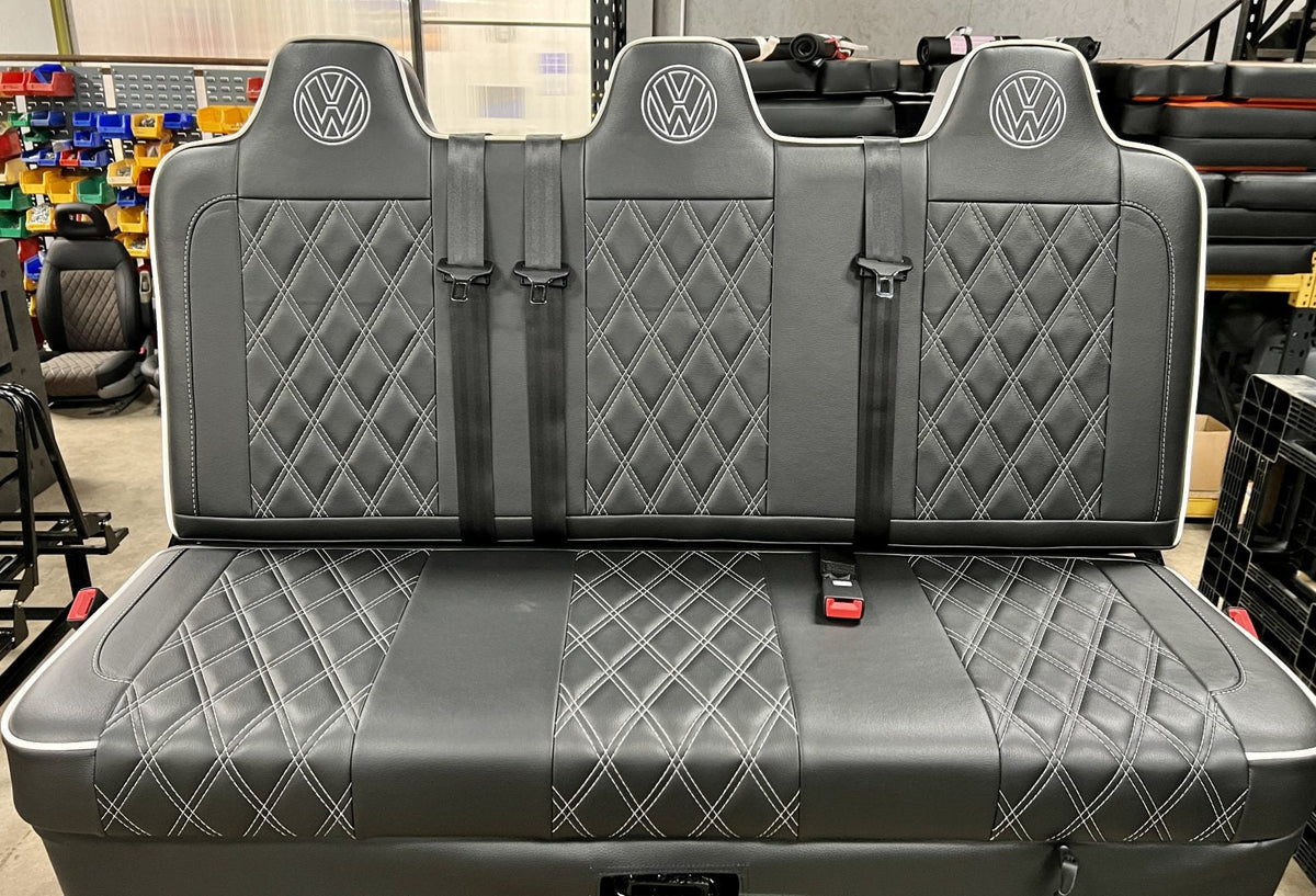 Rock and roll bed full width M1 tested gas assisted legged in black faux Leather with white cross stitching, piping, VW logos and integrated seatbelts.