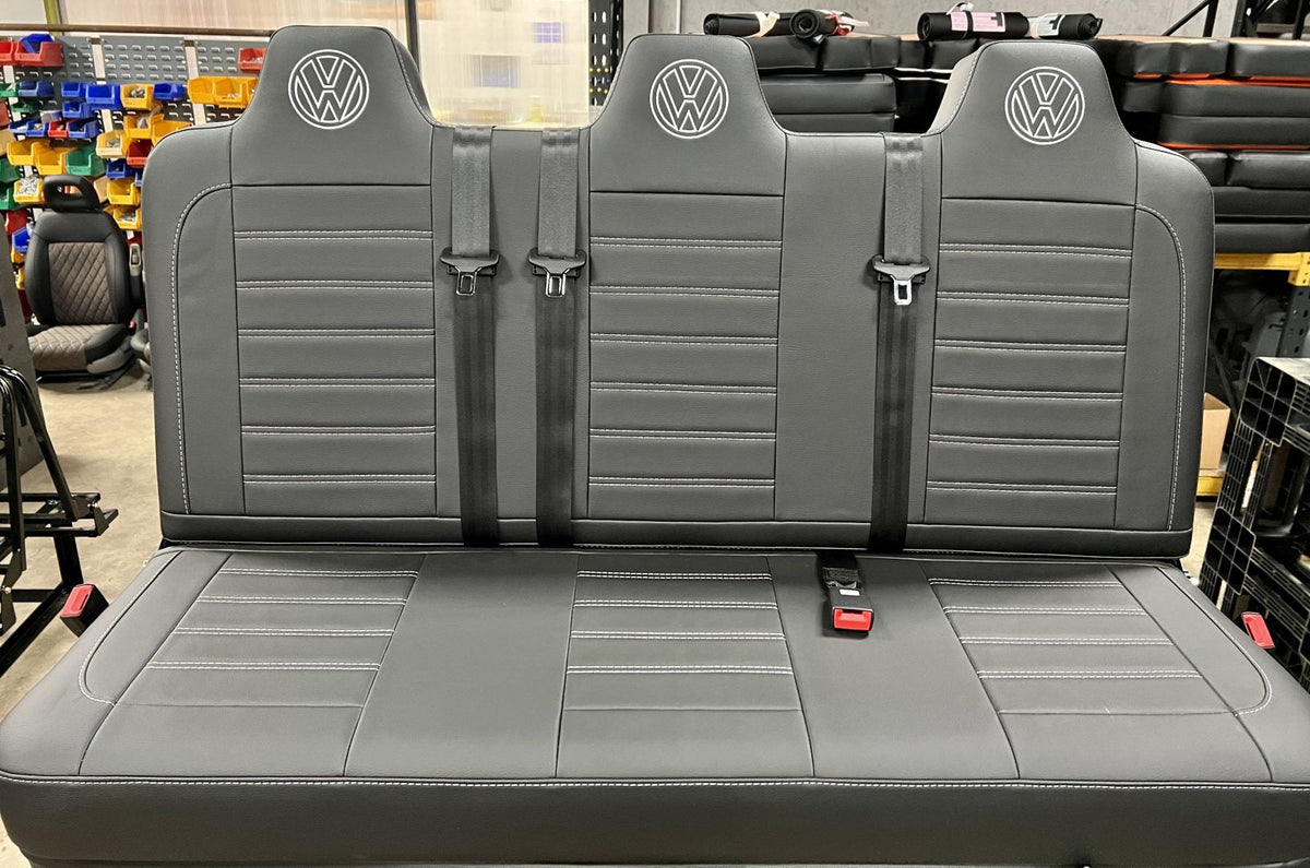 Rock and roll bed full width M1 tested gas assisted legged in black leatherette with light grey stitching, VW logos and integrated seatbelts.
