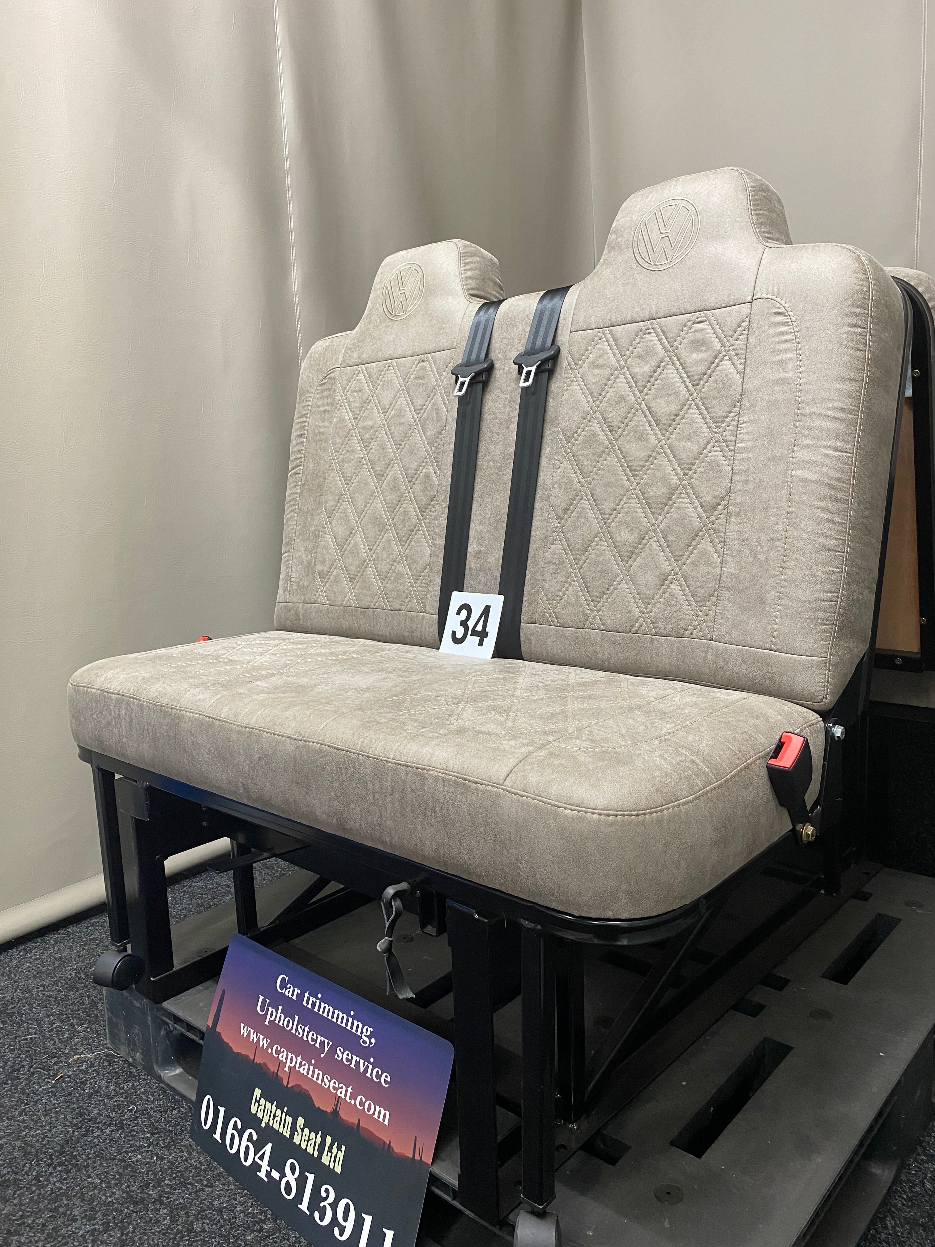 Rock & Roll Bed M1 Tested 3/4 Width, side view of beige faux suede seat with Bentley stitching, VW logos, seatbelts and black metal frame.
