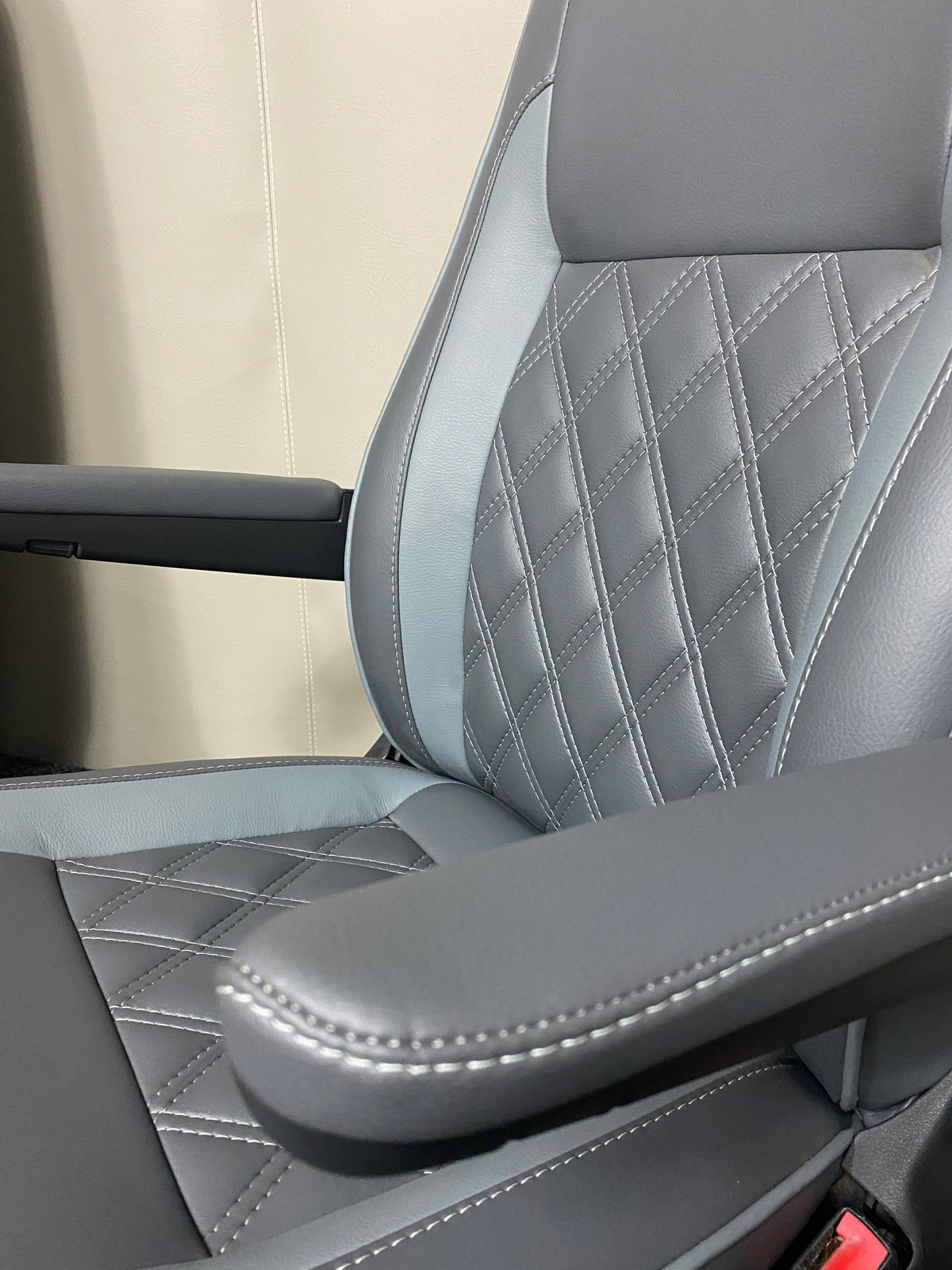 VW Factory Driver Seat T5 T6, close-up angled view of medium grey leatherette with light grey inserts, white Bentley cross stitching, and armrests.