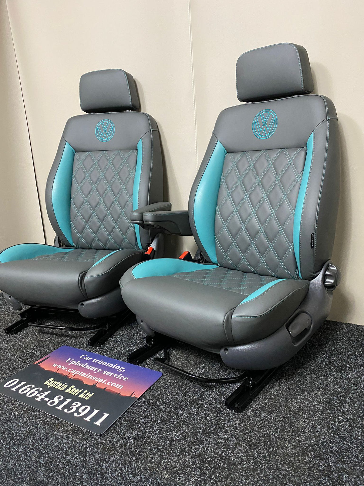 Pair of MK3 Replacement Captain Swivel Seats in grey real leather with teal inserts and horizontal teal stitch pattern, shown from a side angle. Features a VW logo embroidered in teal on the headrests, one armrest per seat.