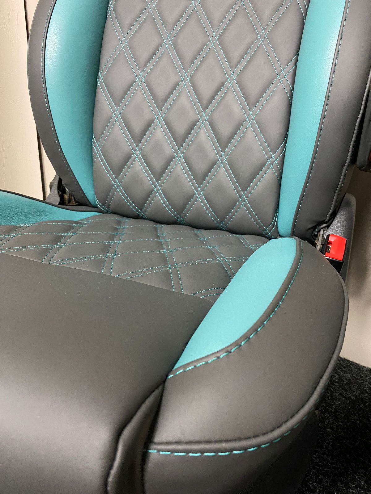 Close-up of MK3 Replacement Captain Swivel Seat, seat base and backrest featuring grey real leather upholstery, teal cross-stitch pattern, teal side inserts.