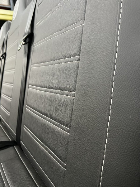 Rock and roll bed full width M1 tested gas assisted legged, angled close-up of the seat back in black leatherette with light grey stitching.
