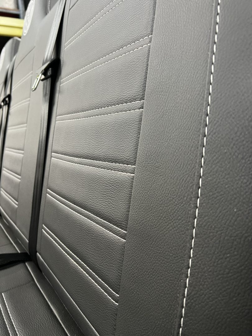 Rock and roll bed full width M1 tested gas assisted legged, angled close-up of the seat back in black leatherette with light grey stitching.