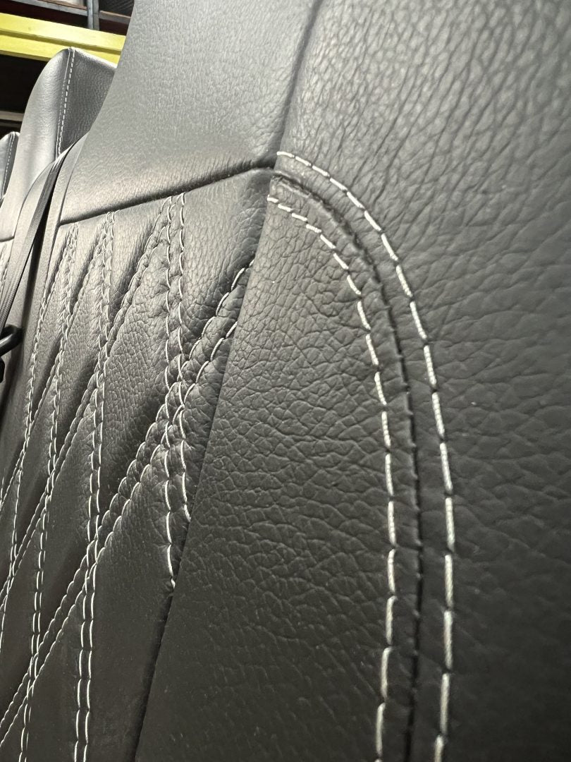 Rock and roll bed full width M1 tested gas assisted legged, close-up of the seat back in black leather with light grey Bentley stitch pattern.