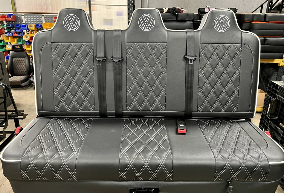 Rock and roll bed full width M1 tested gas assisted legged in black faux Leather with white cross stitching, piping, VW logos and integrated seatbelts.