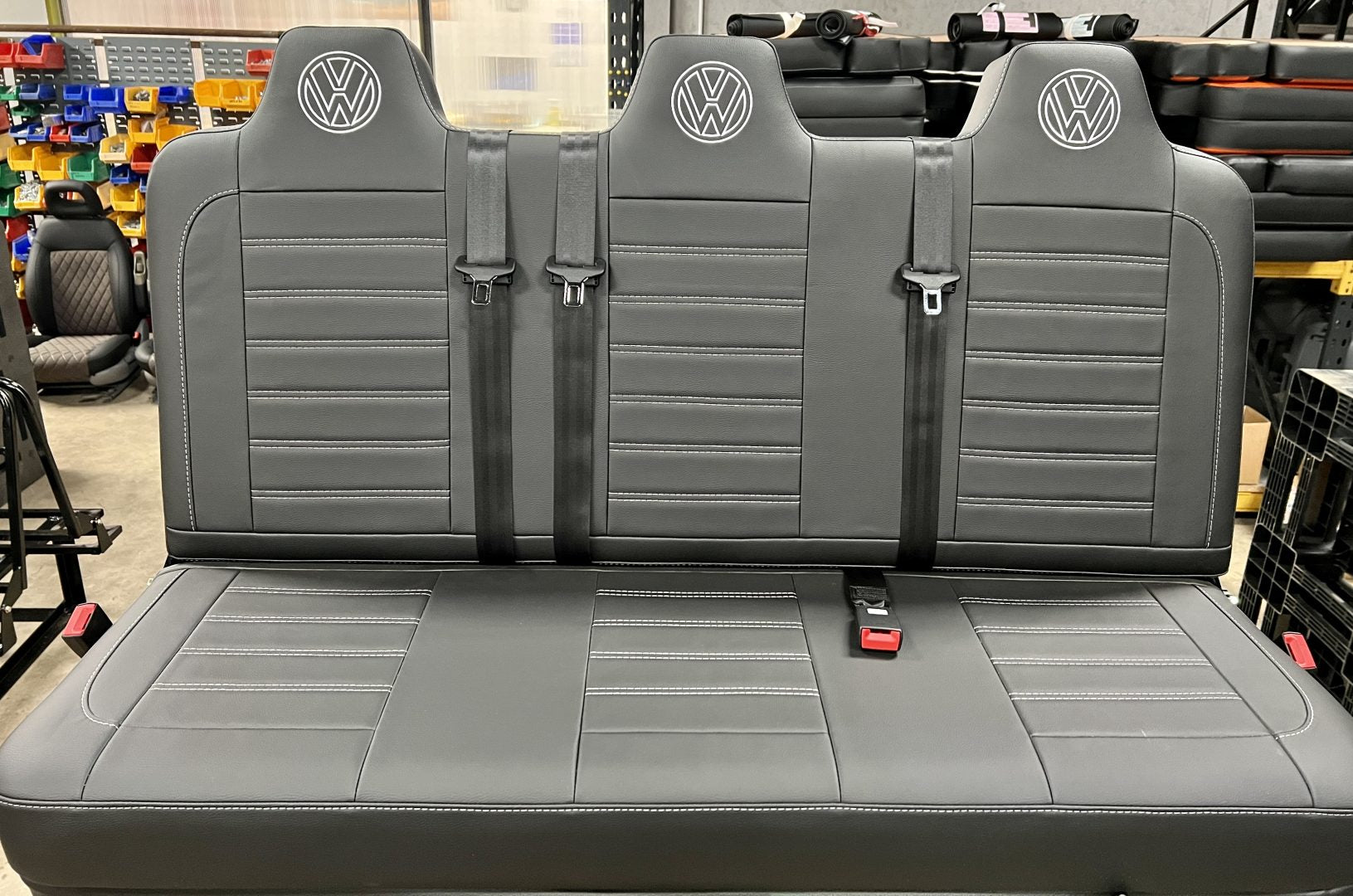 Rock and roll bed full width M1 tested gas assisted legged in black leatherette with light grey stitching, VW logos and integrated seatbelts.