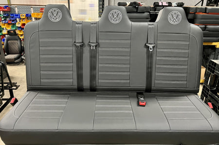Rock and roll bed full width M1 tested gas assisted legged in black leatherette with light grey stitching, VW logos and integrated seatbelts.