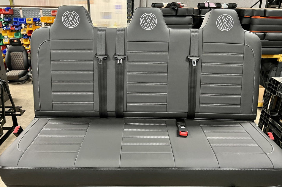 Rock and roll bed full width M1 tested gas assisted legged in black leatherette with light grey stitching, VW logos and integrated seatbelts.
