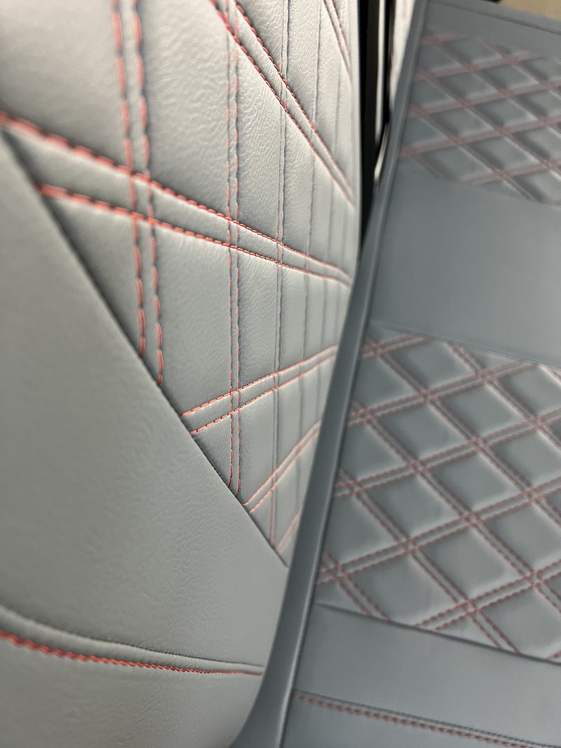 Rock and roll bed M1 tested 3/4 gas assisted legged, close-up of the grey leatherette upholstery with red cross stitching.