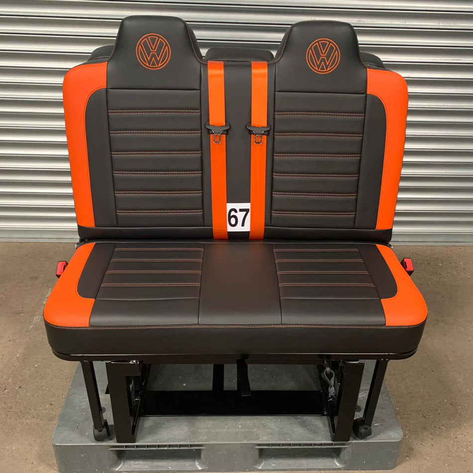Rock and roll bed M1 tested 3/4 gas assisted legged (67) for VW T4 T5 T6 Crafter in black leatherette, with horizontal orange stitching, orange edges, orange seatbelts with VW logos also in orange.