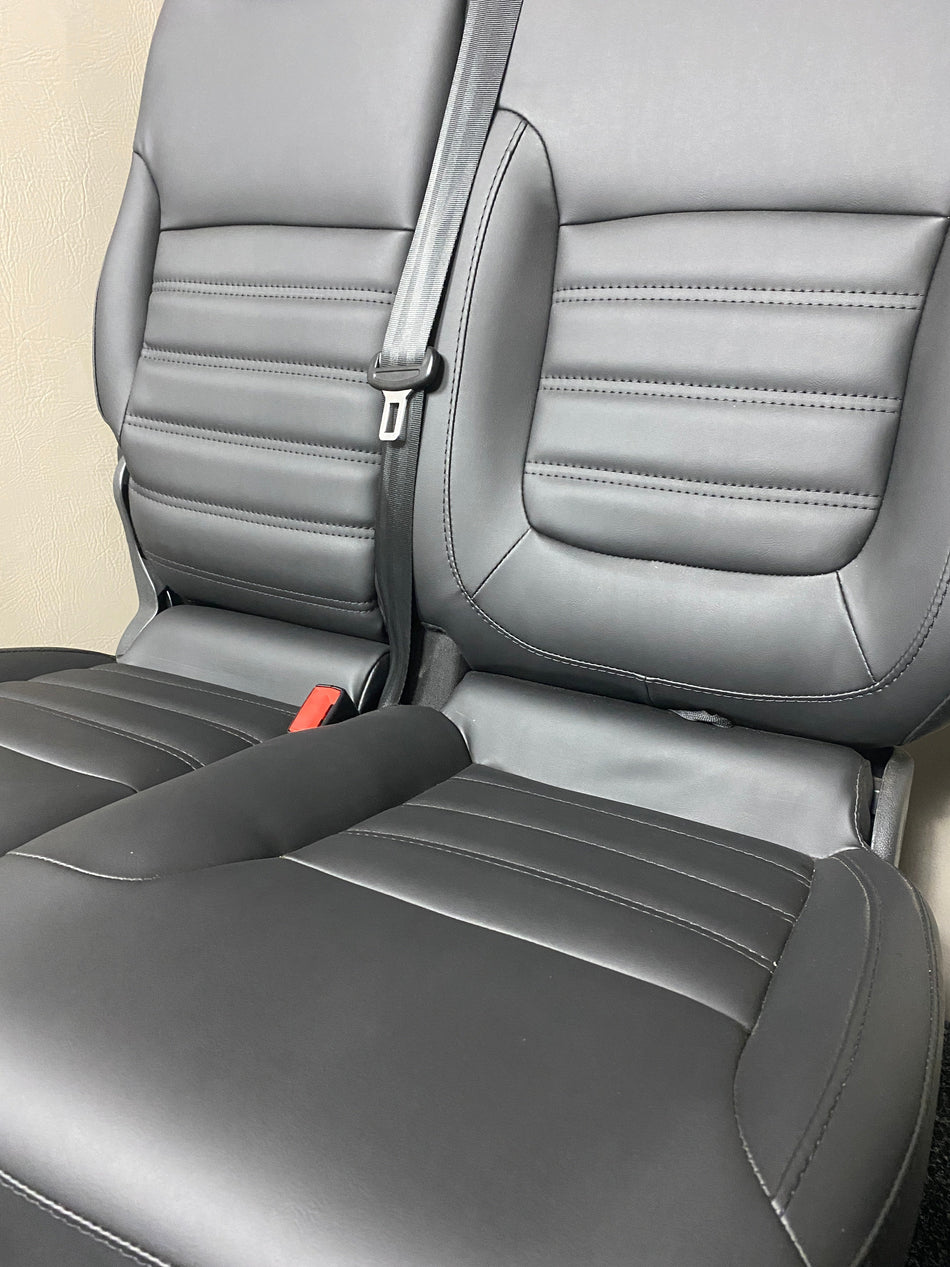 TVP Trafic Vivaro Primastar front seat close-up in black leatherette with black horizontal wide stitching, highlighting the double seat folding backrest and integrated seatbelt.
