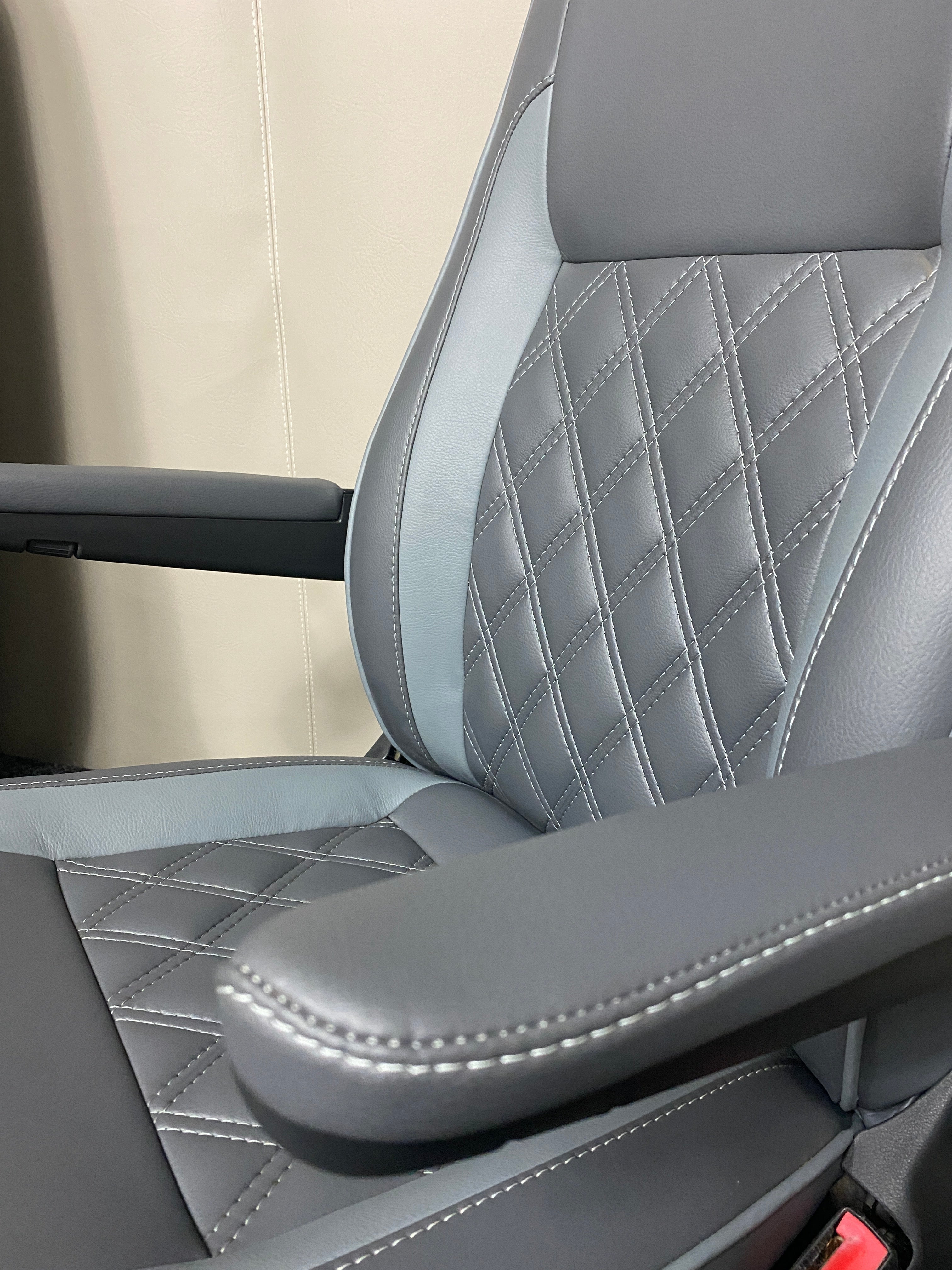 VW Factory Driver Seat T5 T6, close-up angled view of medium grey leatherette with light grey inserts, white Bentley cross stitching, and armrests.