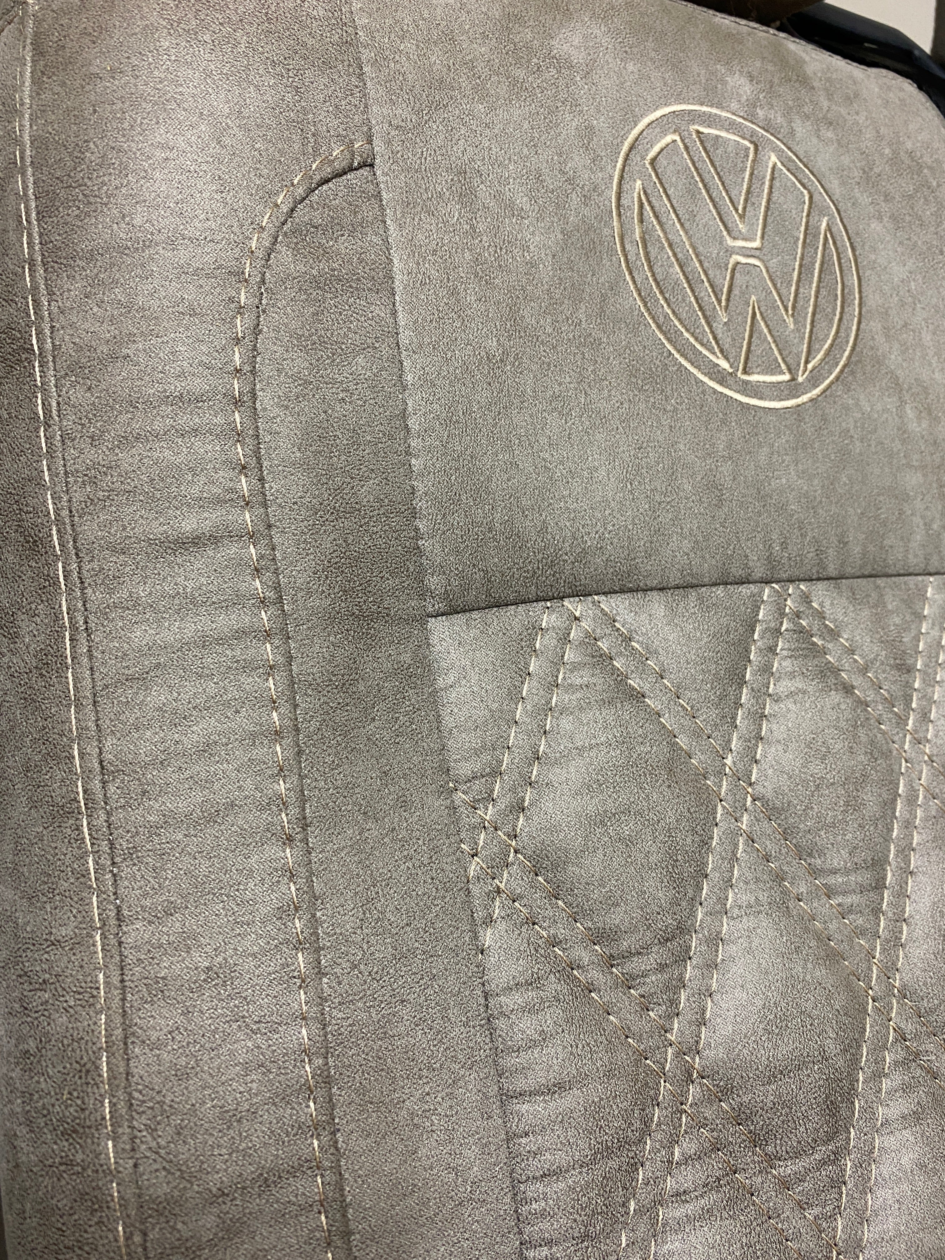 VW Factory Front Seat T5 T6 close-up of the faux suede upholstery with cream Bentley stitching and embroidered VW logo.